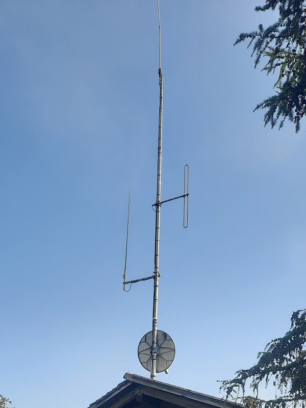 Antennenmast auf dem Hasenberg mit vertikalen Antennen und einer Satellitenschüssel über einem Dach.